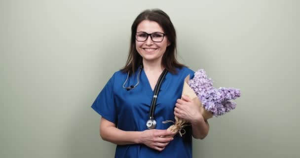 Portret kobiety lekarza pokazujący znak zwycięstwa, szczęśliwy uśmiechnięty medyk z bukietem kwiatów — Wideo stockowe