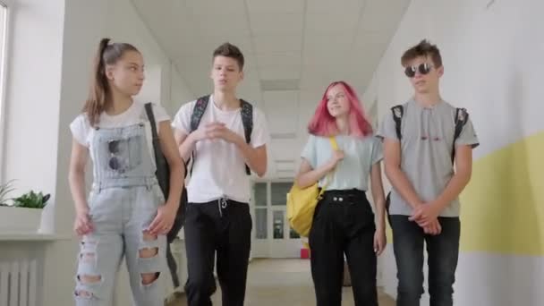 Gruppo di studenti adolescenti che camminano insieme lungo il corridoio scolastico, scolari che sorridono e parlano — Video Stock