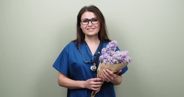 Porträtt av kvinnlig läkare visar dig seger tecken, glad leende läkare med bukett blommor — Stockvideo