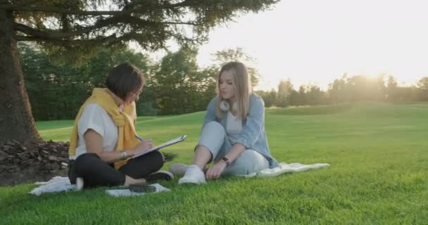 Beraterinnen im Gespräch mit jungen Studentinnen Teenager sitzen auf Rasen im Park auf Gras — Stockvideo