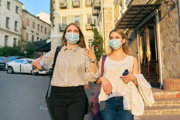 Two young business women in protective medical masks walking together