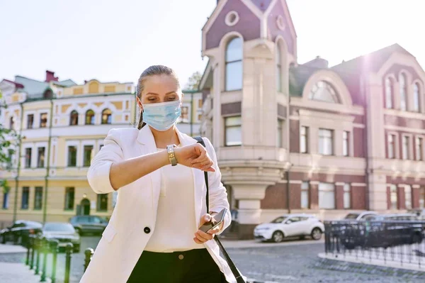 Mujer en máscara médica al aire libre, mirando reloj de pulsera —  Fotos de Stock