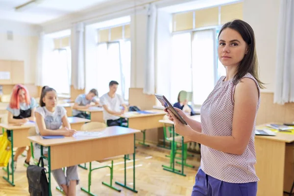 Портрет молодой улыбающейся уверенной женщины-учителя с цифровым планшетом в классе — стоковое фото