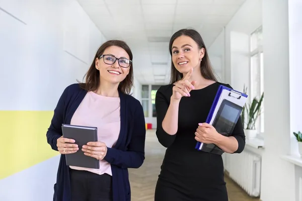Two colleagues of businesswoman walking and talking on corridor