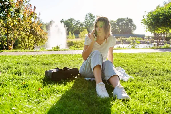 Tråkig ung kvinna som sitter ensam i parken och ringer allvarliga samtal — Stockfoto