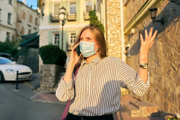 Joven mujer de negocios en máscara de protección médica hablando en el teléfono inteligente al aire libre —  Fotos de Stock