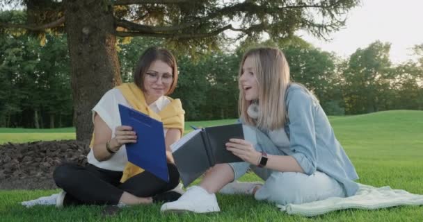 Mulher professora e menina estudante adolescente sentado na grama no parque falando, testando, aprendendo — Vídeo de Stock