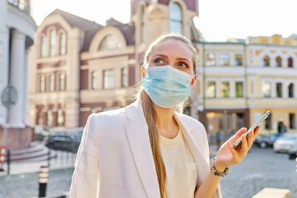 Mujer de negocios joven en máscara de protección médica hablando en el teléfono inteligente —  Fotos de Stock