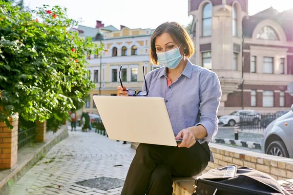 Madura mujer de negocios en la cara máscara de protección médica con ordenador portátil que trabaja al aire libre —  Fotos de Stock