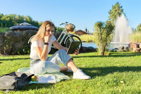 Девушка-подросток сидит с ноутбуком цифровой планшет на зеленой газоне травы в парке — стоковое фото