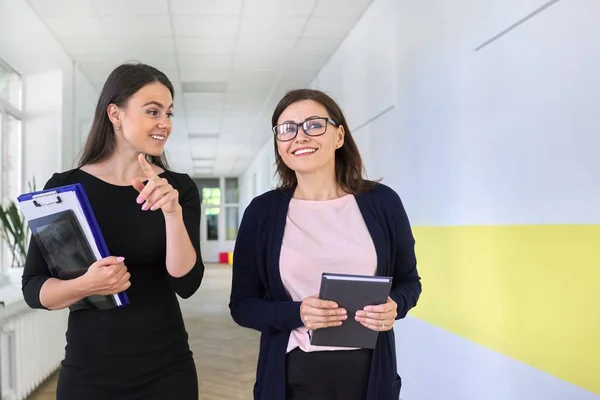 Two colleagues of businesswoman walking and talking on corridor