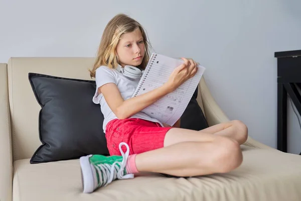 Дитяча дівчина в масці, що сидить на дивані зі шкільним записником — стокове фото