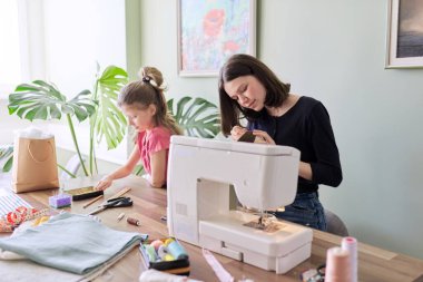 Çocuklar evde oturup oyuncak bebek dikiyorlar.