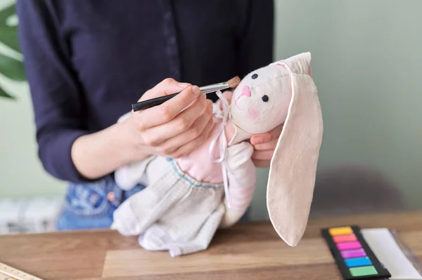 Młoda dziewczyna robi autorom ręcznie robione lalki króliczka, maluje policzki kosmetykami — Zdjęcie stockowe