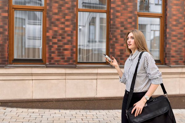 Young business woman walking in city talking on mobile phone