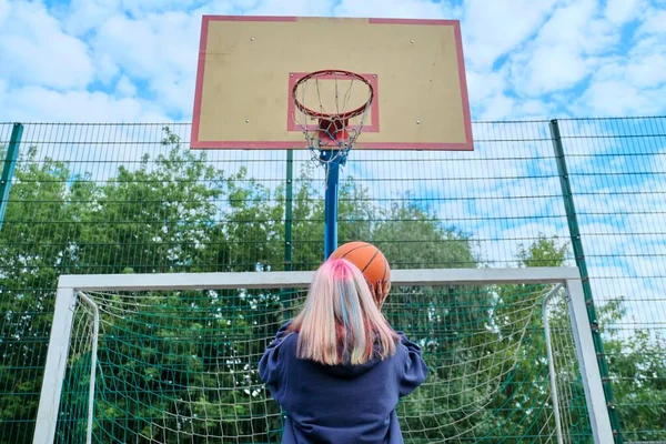 Ragazza adolescente che salta con la palla che gioca a basket di strada, vista posteriore — Foto Stock