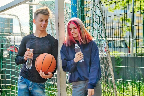 Pár na sportovním basketbalovém hřišti mluvící, stojící s míčem a lahví vody — Stock fotografie