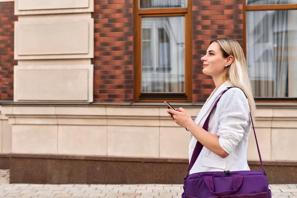 Młoda kobieta biznesu chodzenie z telefonu komórkowego, profil widok przestrzeń kopiowania — Zdjęcie stockowe