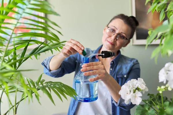 Žena nalévá tekuté minerální hnojivo ve spreji a hnojí rostlinné listy. — Stock fotografie