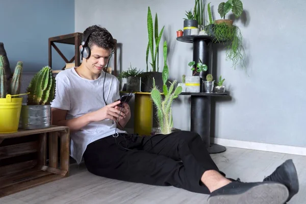 Красивый улыбающийся подросток в наушниках со смартфоном дома — стоковое фото