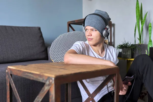 Portrait of hipster teenager in hat with headphones sitting on floor at home — Stock Photo, Image