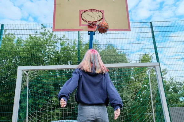 Дівчина-підліток стрибає з м'ячем, граючи в вуличний баскетбол, вид ззаду — стокове фото