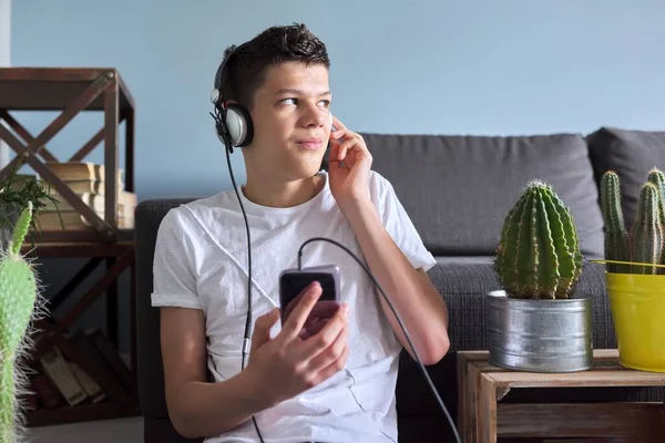 Красивый улыбающийся подросток в наушниках со смартфоном дома — стоковое фото