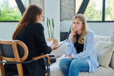 Üzgün genç kadın hasta terapi seansında kadın psikolog psikoterapist, ruh sağlığı danışmanı ve sosyal psikolog ile birlikte ofiste otururken gergin.