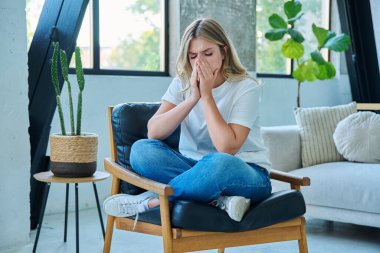 Evdeki sandalyede oturan mutsuz, yorgun, genç bir kadın. Duygusal fiziksel acı çeken üzgün bir kadın. Sorunlar ruhun ve bedenin sağlığı ve gençliğin sorunları
