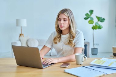 Masasında dizüstü bilgisayarlı ders kitaplarıyla oturan genç bir üniversite öğrencisi. Daktilo yazan defterler. Eğitim, eğitim, gençlik kavramı