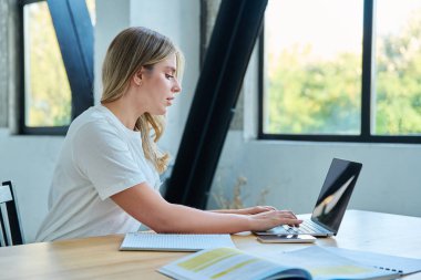 Masasında dizüstü bilgisayarlı ders kitaplarıyla oturan genç bir üniversite öğrencisi. Daktilo yazan defterler. Eğitim, eğitim, gençlik kavramı