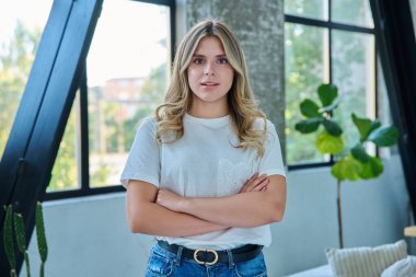 Evin içinde kendine güvenen gülümseyen genç bir kadının portresi. Kollarını kavuşturup kameraya bakan güzel, pozitif 20 'li yaşlarda bir kadın. Güzellik, gençlik, mutluluk, sağlık, yaşam tarzı konsepti