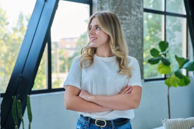 Evin içinde kendine güvenen gülümseyen genç bir kadının portresi. 20 'li yaşlarda güzel bir kadın. Kollarını kavuşturmuş, başka tarafa bakıyor. Profil görüşü var. Güzellik, gençlik, mutluluk, sağlık, yaşam tarzı konsepti