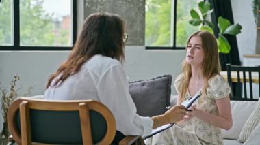 Terapi seansında genç gülümseyen kız hasta psikolog sosyal terapist ile birlikte kanepede oturuyor. Sağlık hizmeti gençlik yardımı, psikolojik hizmetler, psikoterapi