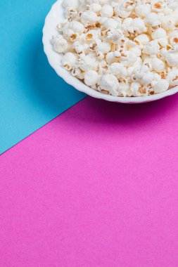 Mavi ve mor arka planda beyaz kase patlamış mısır.