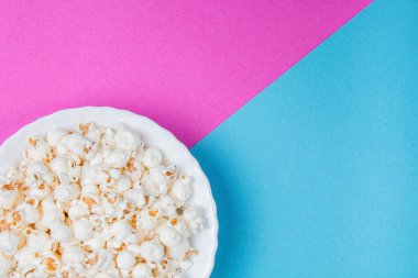 Mavi ve mor arka planda beyaz kase patlamış mısır.