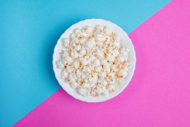 Mavi ve mor arka planda beyaz kase patlamış mısır.