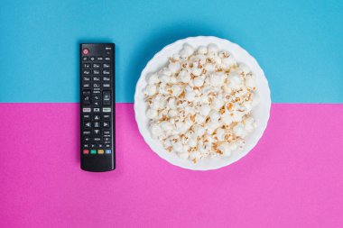 Siyah TV uzaktan kumandalı, mavi ve mor arka planda beyaz patlamış mısır kasesi.