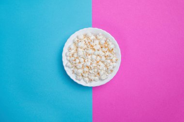 Mavi ve mor arka planda beyaz kase patlamış mısır.