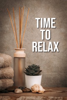 Ahşap bir arka planda kaplıca, mum, taş, havlu ve çiçekler.