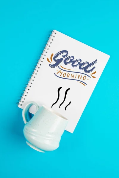 Blue coffee mug on a blue background with the text and a blank white page