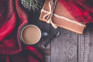 Sıcak kahve kupası, kış günleri için bir eşarba sarılmış, Noel ağacı ve ahşap bir masada hediye.