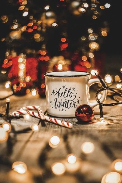 Noel ışıkları ve noel süslemeleri olan beyaz bardağı ahşap bir masaya yakın.