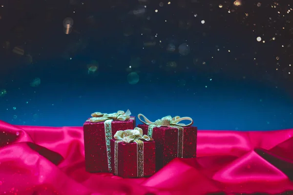 Kırmızı ipek ve mavi arka planda Bokeh ile Noel ışıkları olan parlak kırmızı hediye kutuları.