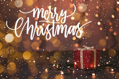 Güzel kırmızı bir hediye kutusunun fotoğrafı, ışık ve Noel alıntılı kar.