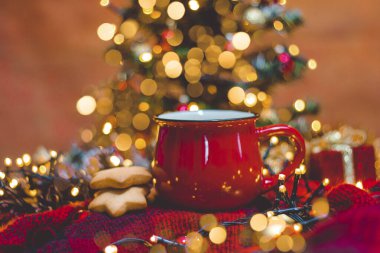 Kırmızı fincan sıcak kahve, Noel ışıkları, taze kurabiyeler ve Noel ağacı.