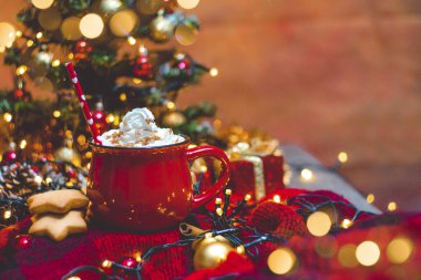 Kırmızı fincan sıcak kahve, Noel ışıkları, taze kurabiyeler, krema, tarçın ve saman.