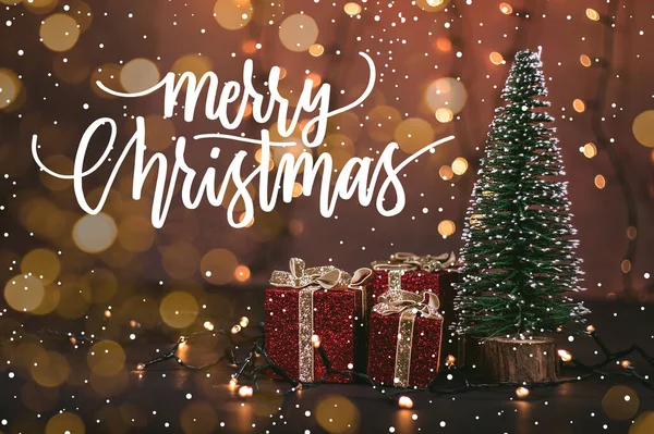 Güzel paketlenmiş hediyelerle dolu bir Noel ağacının fotoğrafı. İçinde Noel alıntısı olan ışıklar ve kar.