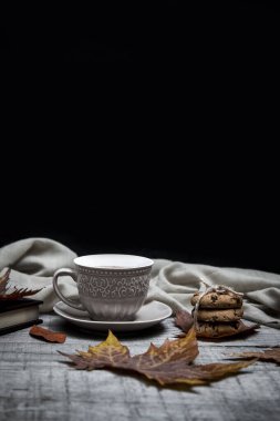 Bir fincan sade kahve ve çikolatalı kurabiyeler. Etrafı sonbahar yaprağı ve ahşap bir masada defter ile çevrili.