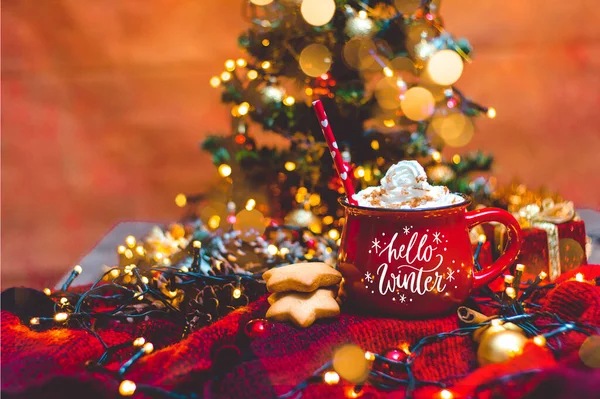 Kırmızı fincan sıcak kahve, Noel ışıkları, taze kurabiyeler, krema, tarçın ve saman.